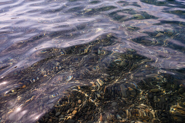 Underwater pebble backgrounds. Colorful stones sea bottom in the sun rays. View from above through clear water. Seascape wallpaper texture. Defocus.