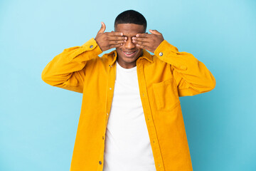 Young latin man isolated on blue background covering eyes by hands and smiling