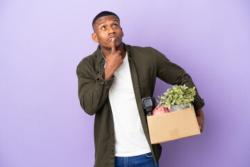 Latin man making a move while picking up a box full of things having doubts while looking up