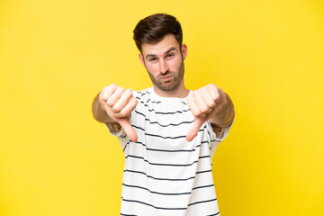 Young caucasian man isolated on yellow background showing thumb down with two hands