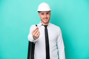 Young architect caucasian man with helmet and holding blueprints isolated on blue background making...