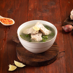 A bowl of fish soup with chili sauce on a wooden background
