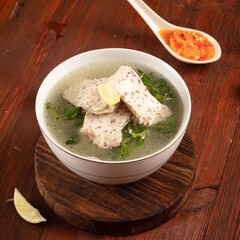 A bowl of fish soup with chili sauce on a wooden background