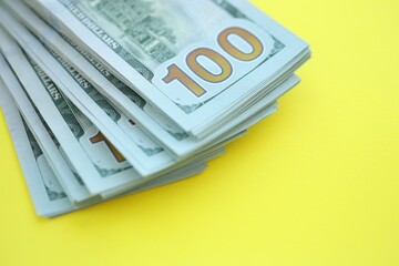 Big amount of hundred dollar bills in thick stack lies on bright yellow color paper background