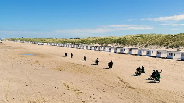 Drone follows a small group of people driving mopeds on a beach