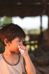 Young boy holding a blood-stained tissue to his nose in a shaded outdoor area with soft natural light.