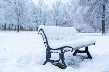 A lonely empty bench covered in a thick layer of fresh snow in a snowy park or forest.