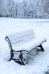 A lonely empty bench covered in a thick layer of fresh snow in a snowy park or forest.