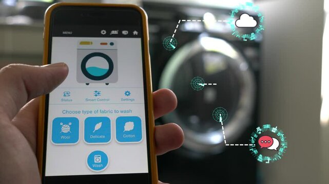 A person is holding a cell phone that is displaying a laundry room. The phone is showing a bed and a washing machine