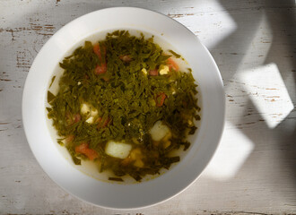 Fresh green soup brimming with vegetables garnished with herbs on a rustic wooden table