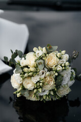 a bouquet of flowers lying on a dark surface. The bouquet consists of white and cream roses, as well as buds and greenery. Eucalyptus leaves add green accents to the composition.