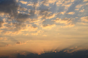 Golden rays burst through clouds at sunset over tranquil landscape