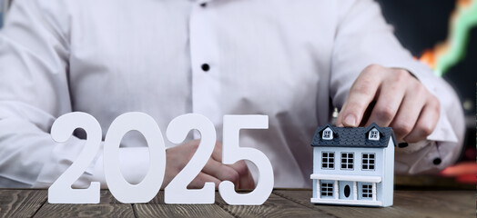 2025 Real Estate Vision: Hands Holding a Model House with Stock Market Charts in the Background for...