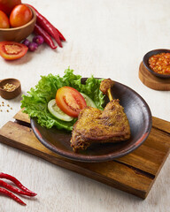 indonesian traditional ayam greprek, a fried chicken with sambal chili sauce on top of it, on a white wooden background.
