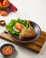 indonesian traditional ayam greprek, a fried chicken with sambal chili sauce on top of it, on a white wooden background.