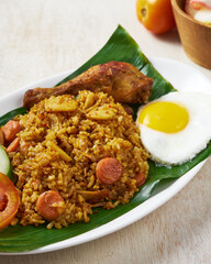 Indonesian fried rice with fried chicken and sunny side up egg on a banana leaves in white wooden background.
