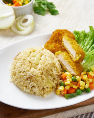 Fried chicken katsu with butter rice and vegetable, in a white plate on a wooden background
