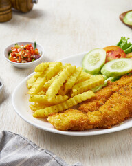 Fried fish and chips with vegetable pickles, in a white plate on a white wooden background
