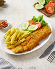 Fried fish and chips with vegetable pickles, in a white plate on a white wooden background
