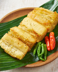 Indonesian fried cassava with green and red chili, on top of banana leaves on a wooden plate in a white wooden background.