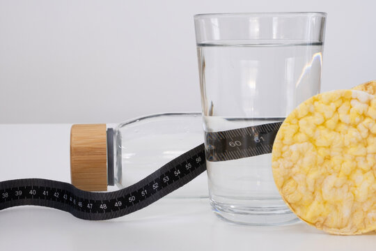 A health and fitness themed image featuring a glass of water, a reusable water bottle with a wooden cap, and a black measuring tape with the number 60cm prominently displayed.