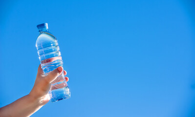 A girl holds a bottle of drinking water in her hand against a blue sky background
