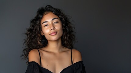 Naklejka premium Beautiful young woman with long dark curly hair and light makeup wearing a black off-the-shoulder dress smiling at the camera.