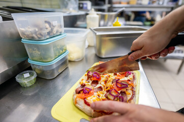 A chef slices a freshly prepared pizza topped with sausage, cheese, and onions in a restaurant...