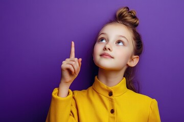 Obraz premium A young girl points upwards with her finger, curious and engaged