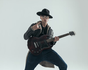 cool young man making rock and roll gesture while playing electric guitar