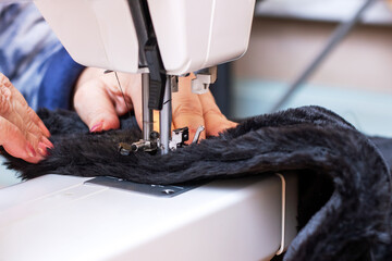 A woman is diligently sewing a piece of black fur on her sewing machine