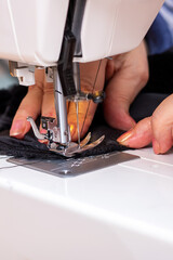 A woman is diligently sewing a piece of black fur on her sewing machine