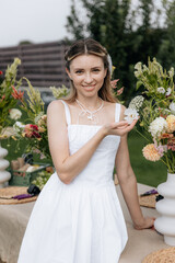 Portrait of a beautiful girl in a white dress with flowers in the garden on a lawn background in...