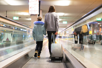 Mother and son walking on moving walkway at airport terminal holding hands
