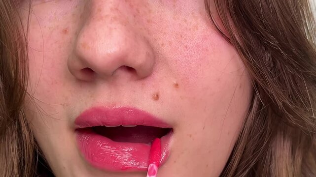 Closeup of woman pressing lips together pink lipstick pink lip gloss on young lips of girl with dark brown hair cosmetics close-up angle kiss