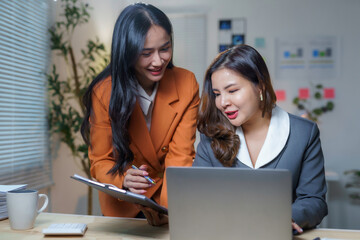 Businesswomen working together analyzing financial data using laptop and clipboard in modern office