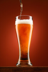 pouring beer into glass, wooden stand, red background, close-up view of object, beer foams and bubbles