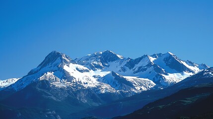 Fototapeta premium A mountain range with snow-covered peaks under a clear blue sky.