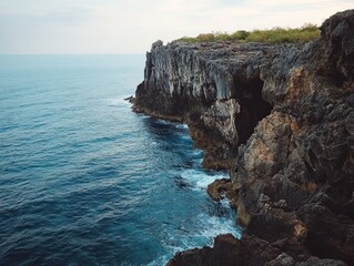 Majestic rocky cliffs meet the vast ocean with a touch of green foliage on top