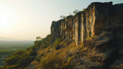 Fototapeta premium Scenic view of a cliff face with a carving and a lush green forest in the background at dawn