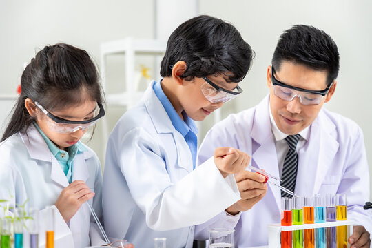 Asian boy and girl children pupils conducting colorful chemistry experiments with male teacher in lab