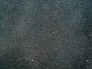 A textured dark surface with subtle variations and specks, resembling asphalt or concrete.