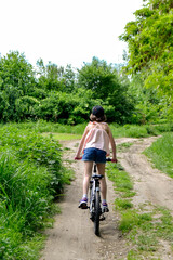 Young girl cyclist enjoy the beautiful sunrise on summer forest trail. Close-up portrait of a happy little girl in a helmet on a bicycle. High quality photo