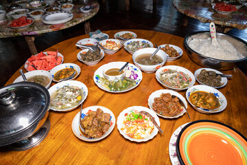 A set of various Burmese curries on the wooden table. Various meat curries, rice, fried fruits, and vegetables.