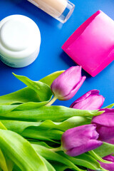 Stylish Mother's Day gift idea. Top view flat lay of high-heels, handbag, gift box, tulip flowers, lipstick, makeup brushes, and earrings on a pastel beige background with open envelope with postcard