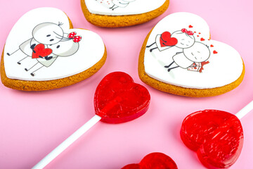 Gingerbread cookies and red heart-shaped lollipops for Valentine's Day on a pink background, sweet Valentine's Day gift, cookies with cream and icing, banner