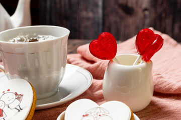 tea in a white porcelain cup and saucer, next to gingerbread cookies with white glaze, red heart-shaped lollipops, Valentine's Day composition, Valentine's Day tea party, bouquet of multi-colored gyps