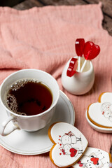 tea in a white porcelain cup and saucer, next to gingerbread cookies with white glaze, red heart-shaped lollipops, Valentine's Day composition, Valentine's Day tea party, bouquet of multi-colored gyps