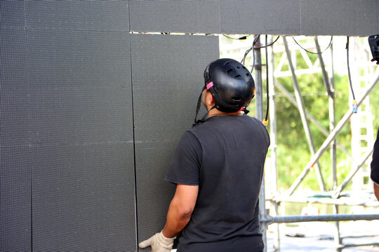
Technician working on stage assembling giant LED screen panels for rock event. Man working on music show production.