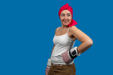 Confident mature woman wearing pink boxing gloves and headscarf, fighting against cancer